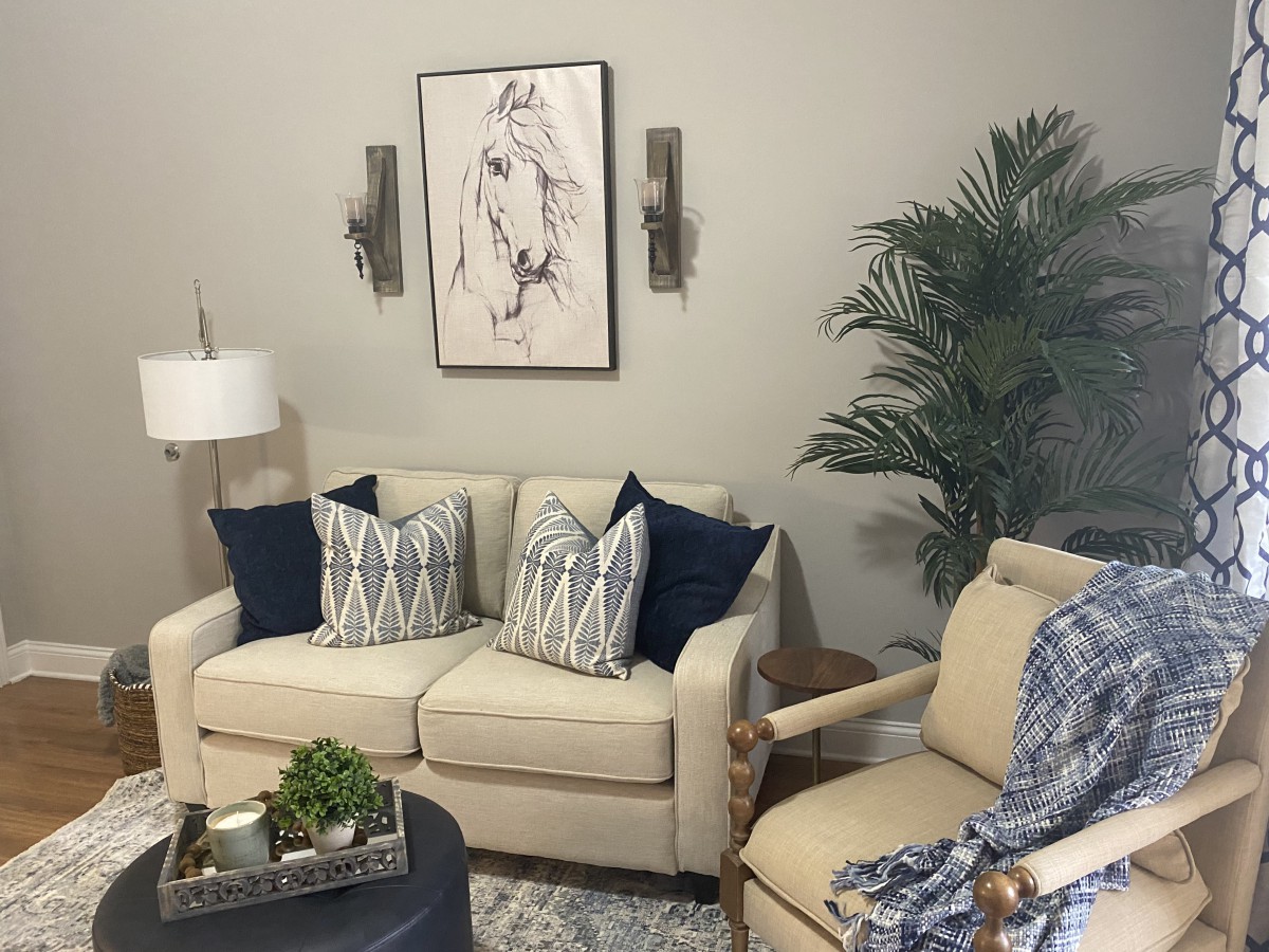 A cozy living room with a beige sofa, decorative cushions, wall art, and greenery.