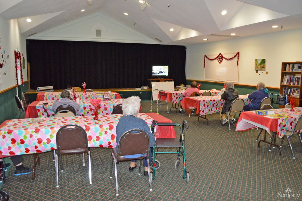 A community gathering with elderly participants seated at decorated tables in a hall.