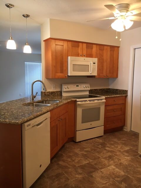 A modern kitchen featuring wood cabinets, granite countertops, and white appliances.