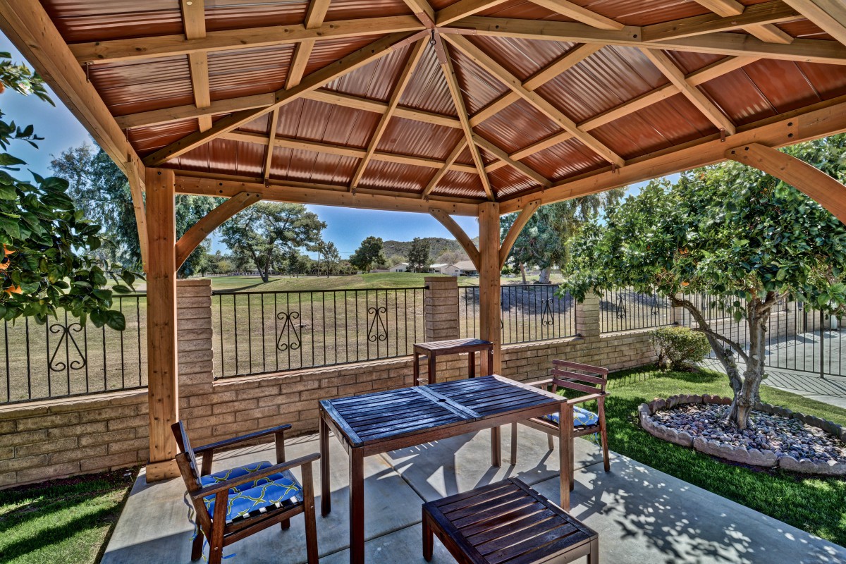 A cozy gazebo with seating in a sunny backyard garden.
