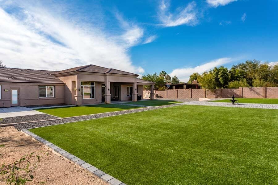 A modern residential house with a large, well-maintained lawn under a clear blue sky.
