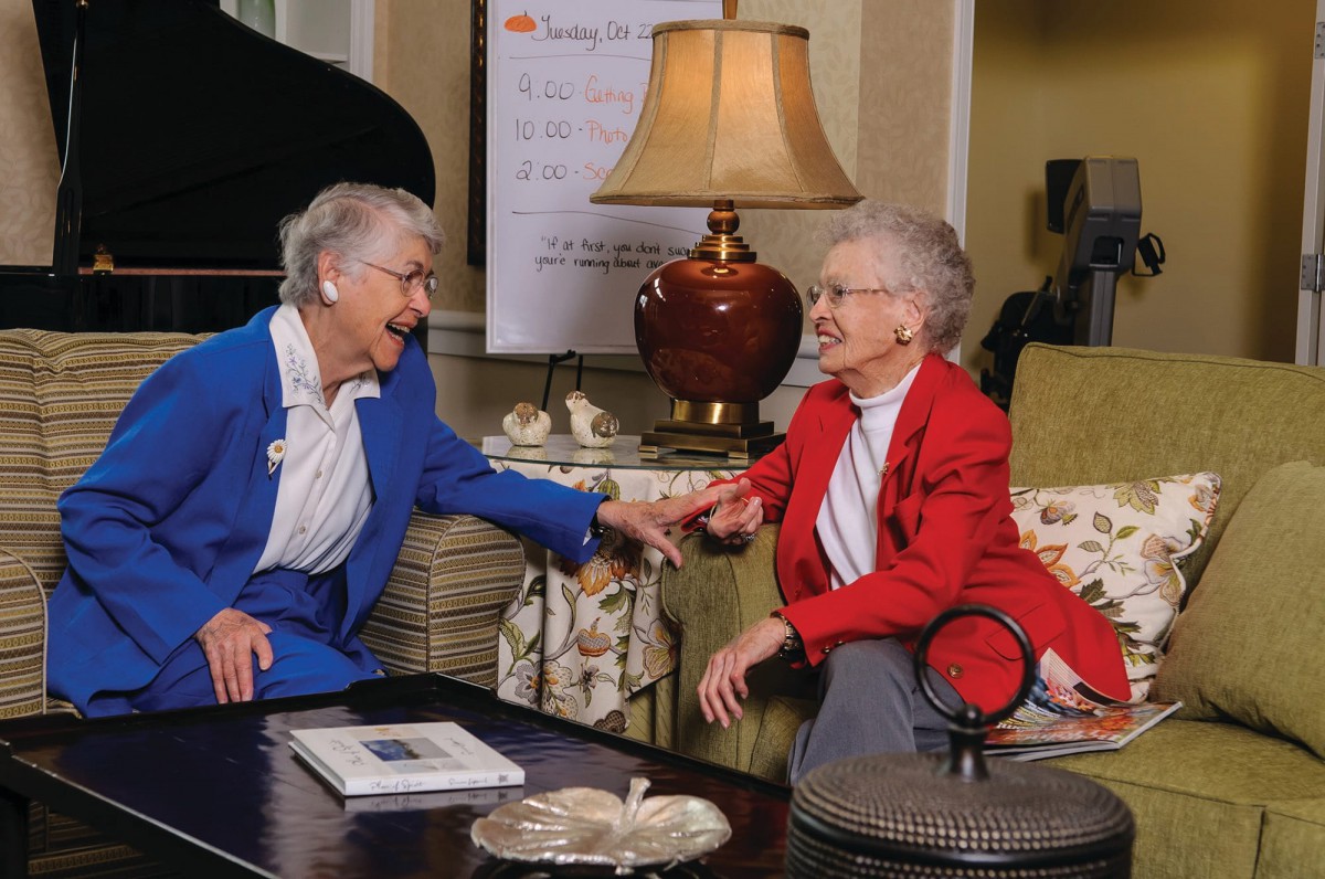 Two elderly women share a joyful conversation in a cozy living room setting.
