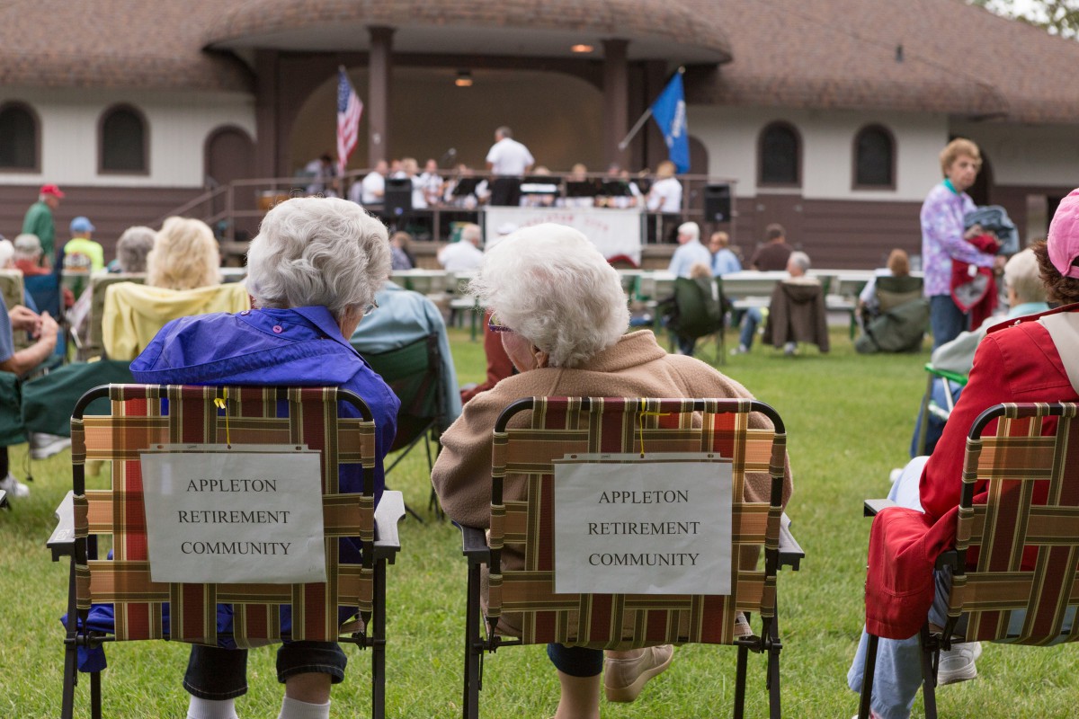 Elderly individuals enjoying an outdoor music performance at a community event.
