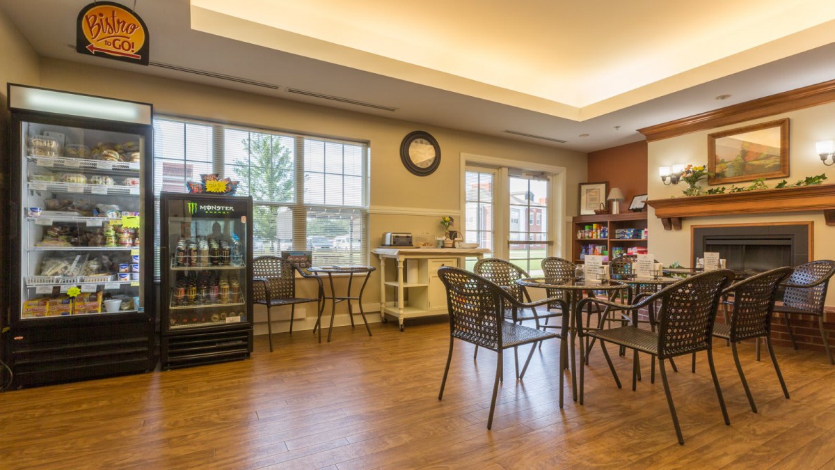 A cozy cafe interior with tables and chairs, featuring large windows that let in natural light.