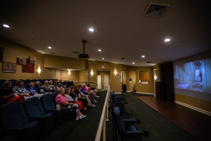 An audience seated in a theater watching a presentation on a screen.