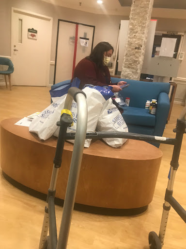 A person sitting in a waiting area surrounded by bags, wearing a mask.
