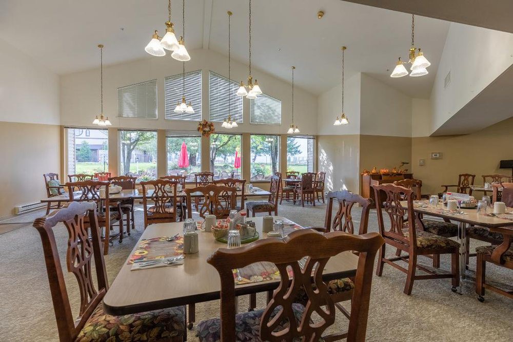 An empty dining room with tables and chairs, featuring large windows and ceiling lights.