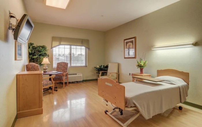 A clean and organized hospital room with a single bed, chair, table, and window.