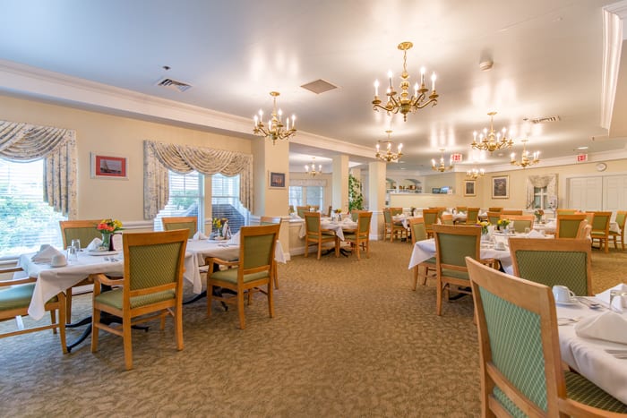 An elegant dining room with well-arranged tables and chairs, illuminated by chandeliers.