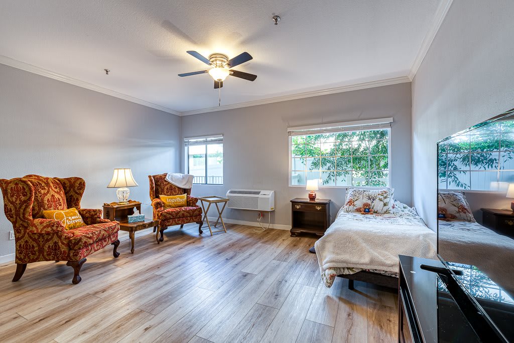 A spacious bedroom with wooden flooring, featuring a bed, comfortable chairs, and a ceiling fan.