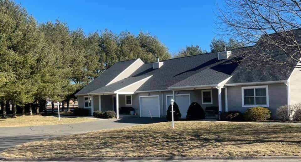 A suburban residential house with a driveway and surrounding trees on a sunny day.