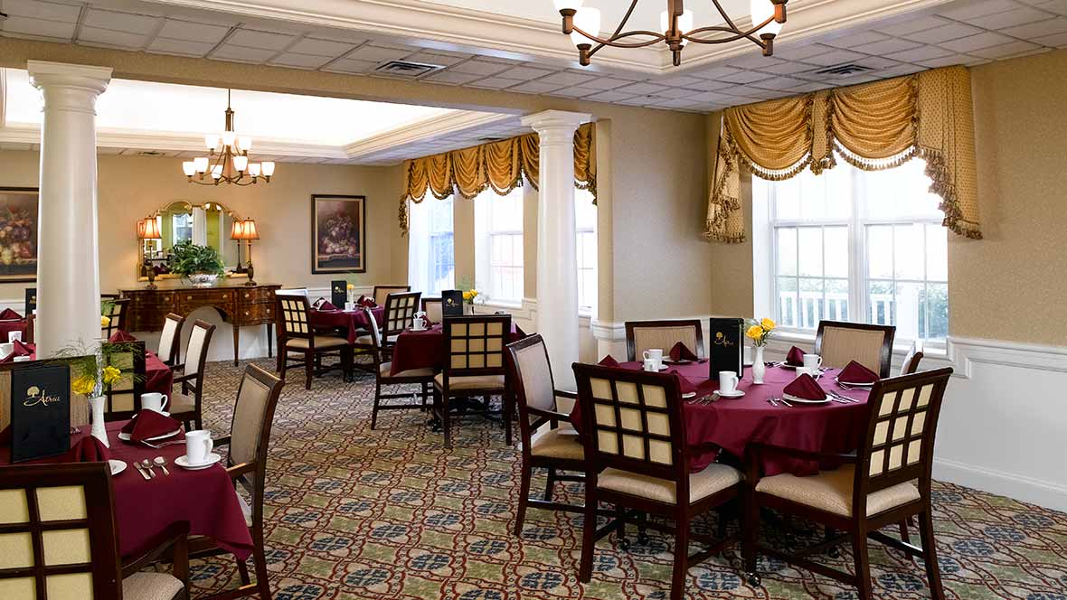 An elegant dining room with neatly arranged tables and chairs, featuring large windows, chandeliers, and decorative curtains.