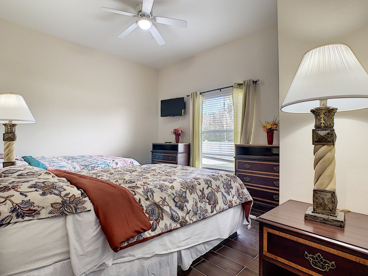 A cozy bedroom with a neatly made bed, side table with a lamp, and a dresser by the window.