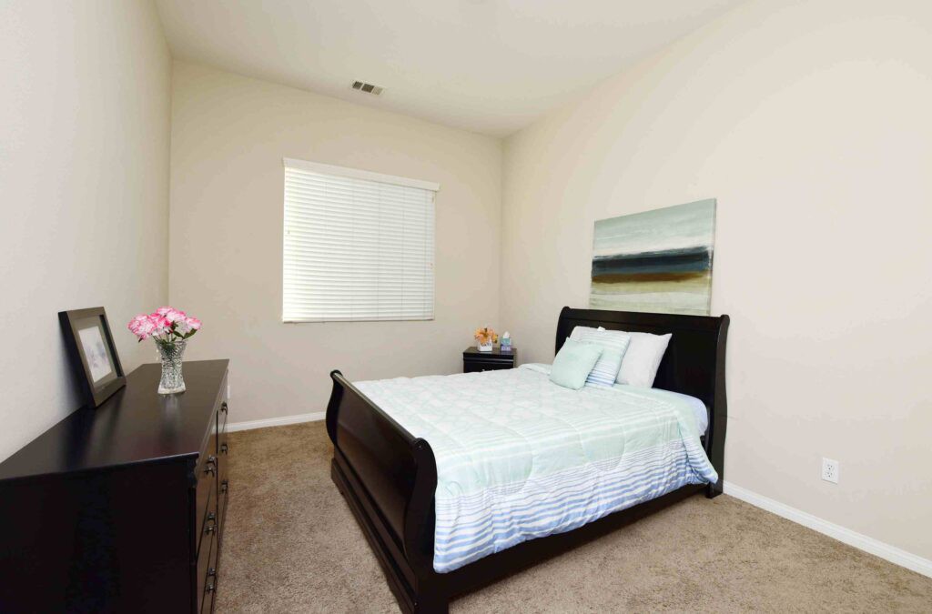 A neatly arranged bedroom with a bed, dresser, and artwork on the wall.