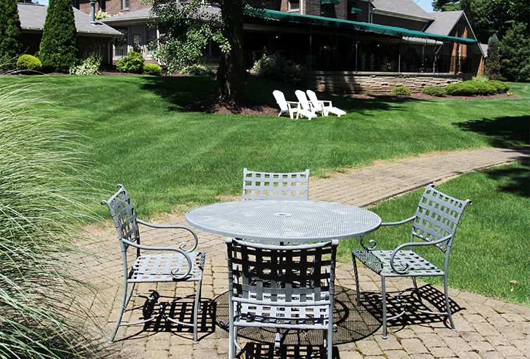 A patio set with a table and chairs on a brick surface, overlooking a lush green lawn.