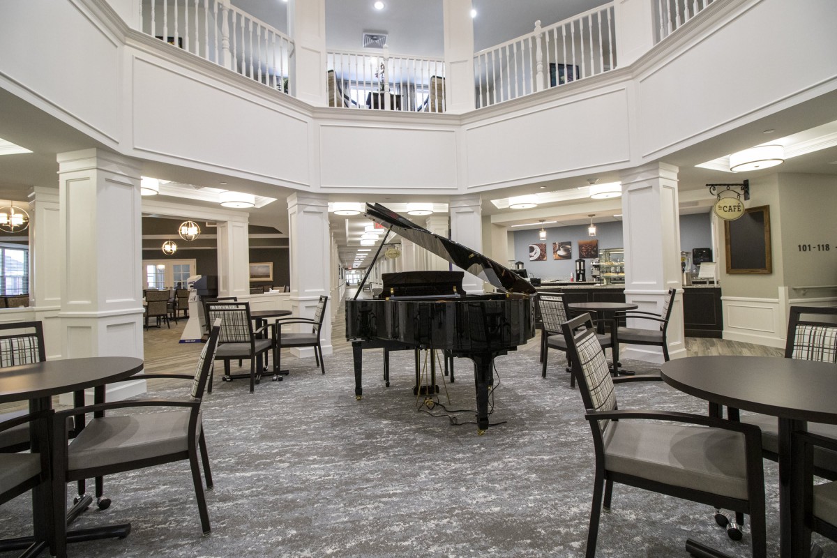 A grand piano is centrally placed in a stylish lobby area with chairs arranged around it.