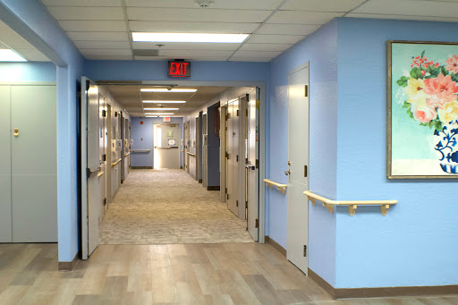 A well-lit corridor in a healthcare facility with blue walls and multiple doors leading to patient rooms.