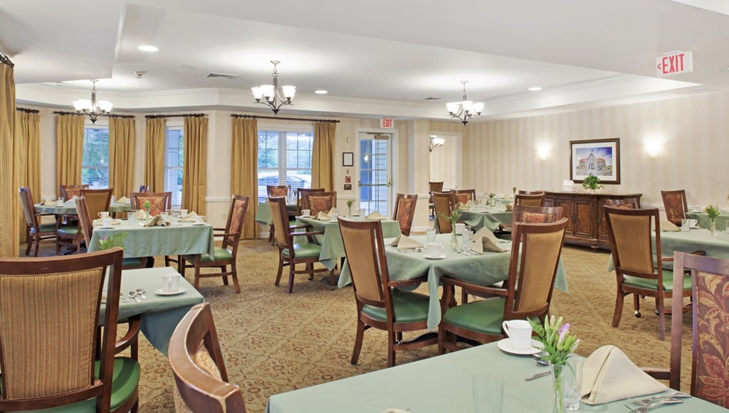 A well-lit dining area with green tablecloths and neatly arranged tables and chairs.