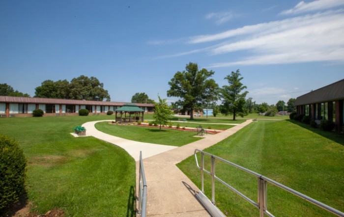 A scenic view of a park with winding walkways, manicured lawns, and trees under a clear blue sky.