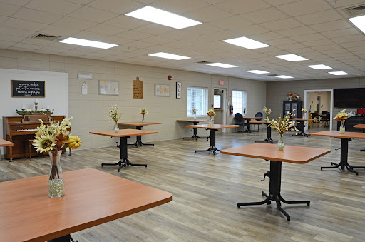 A spacious and well-lit event room set up with tables and decorative flowers.