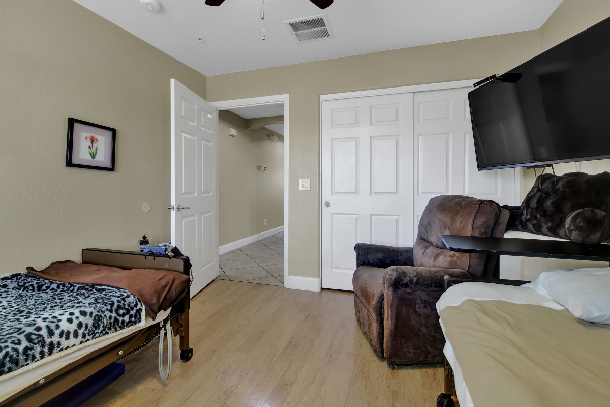 A well-furnished bedroom featuring a bed, recliner chair, wall-mounted TV, and an open closet door.