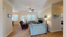 A cozy living room with comfortable seating, a ceiling fan, and large windows.