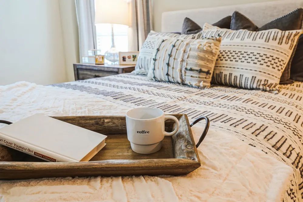 A cozy bedroom setup with a decorative tray holding a mug and notebook on the bed.