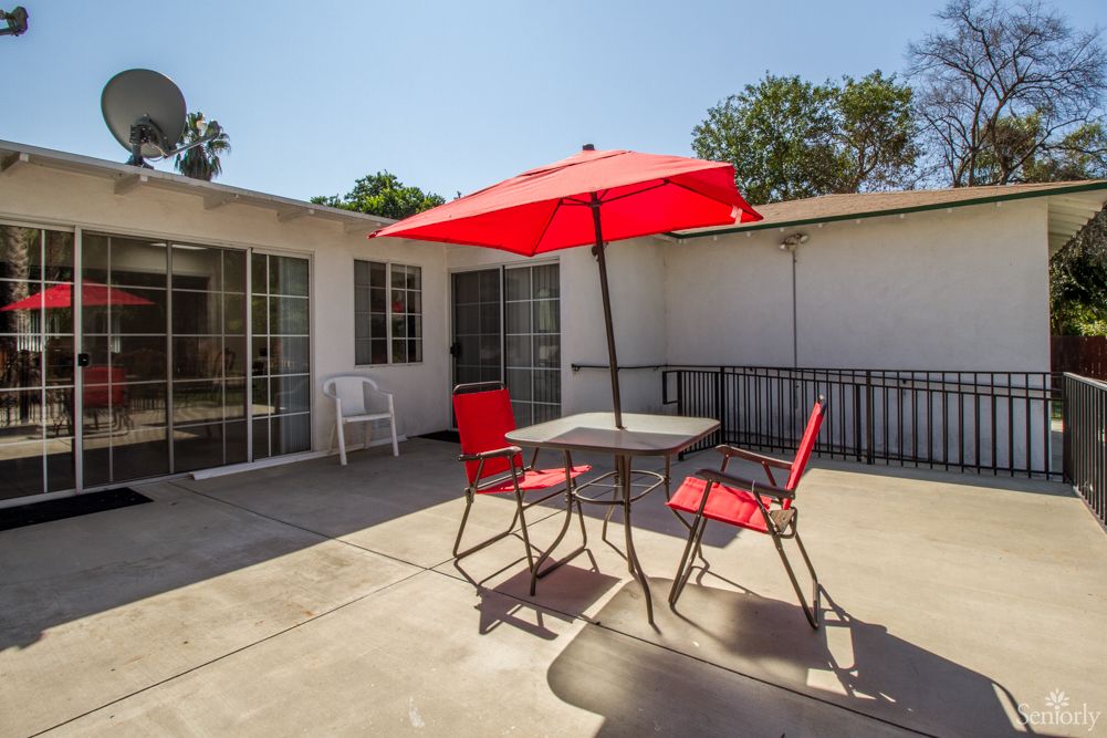 A sunny patio with a red umbrella, table, and chairs.