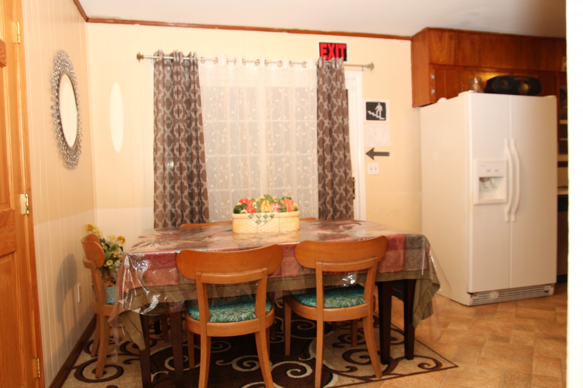 A cozy dining area with a table set for four, featuring decorative curtains and a nearby refrigerator.