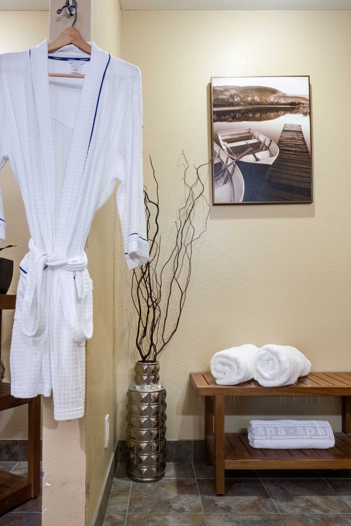 A serene spa setting with a white robe, rolled towels on a bench, and decorative elements.