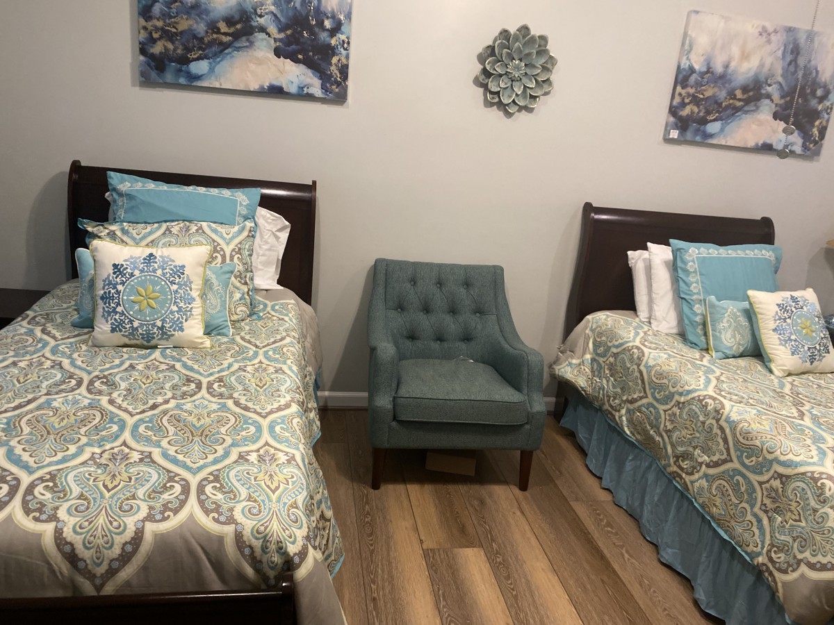 A cozy bedroom with two twin beds, featuring blue and white patterned bedding and a teal armchair in between.