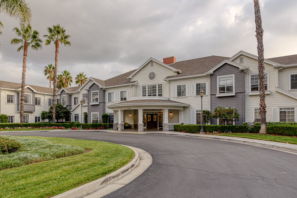 A residential building with a circular driveway, surrounded by palm trees on a cloudy day.