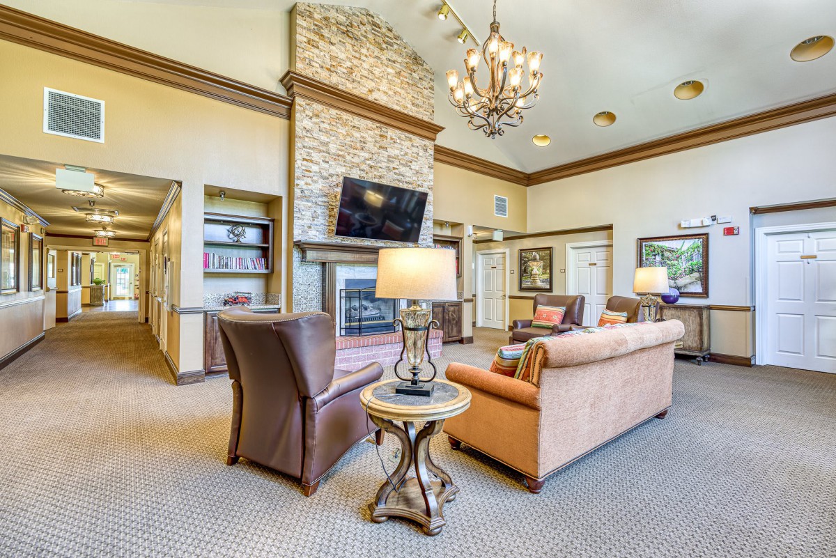 A spacious and elegantly decorated living room featuring a stone fireplace, comfortable sofas, a large chandelier, and a flat-screen television.