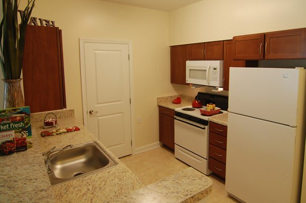 A small kitchen with wooden cabinets and standard appliances, including a stove, refrigerator, microwave, and sink.