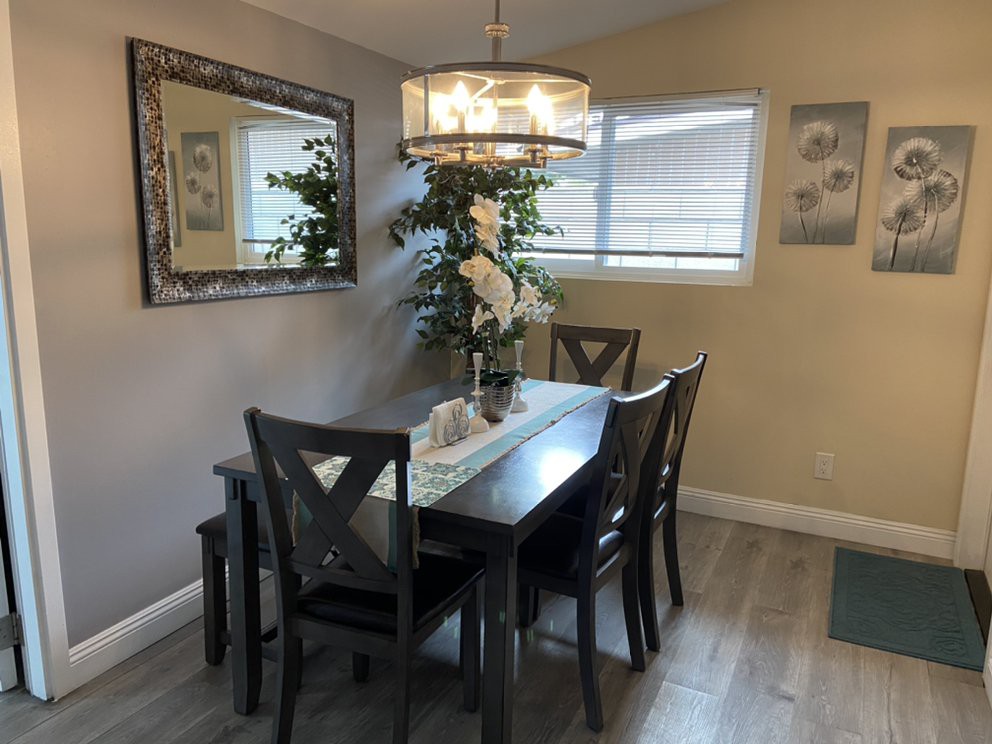 A stylish dining room with a dark wooden table and chairs, illuminated by a chandelier, featuring a large mirror and indoor plants.