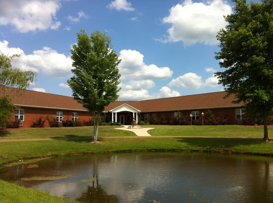 A serene view of a building with a pond in the foreground and a clear sky with scattered clouds.