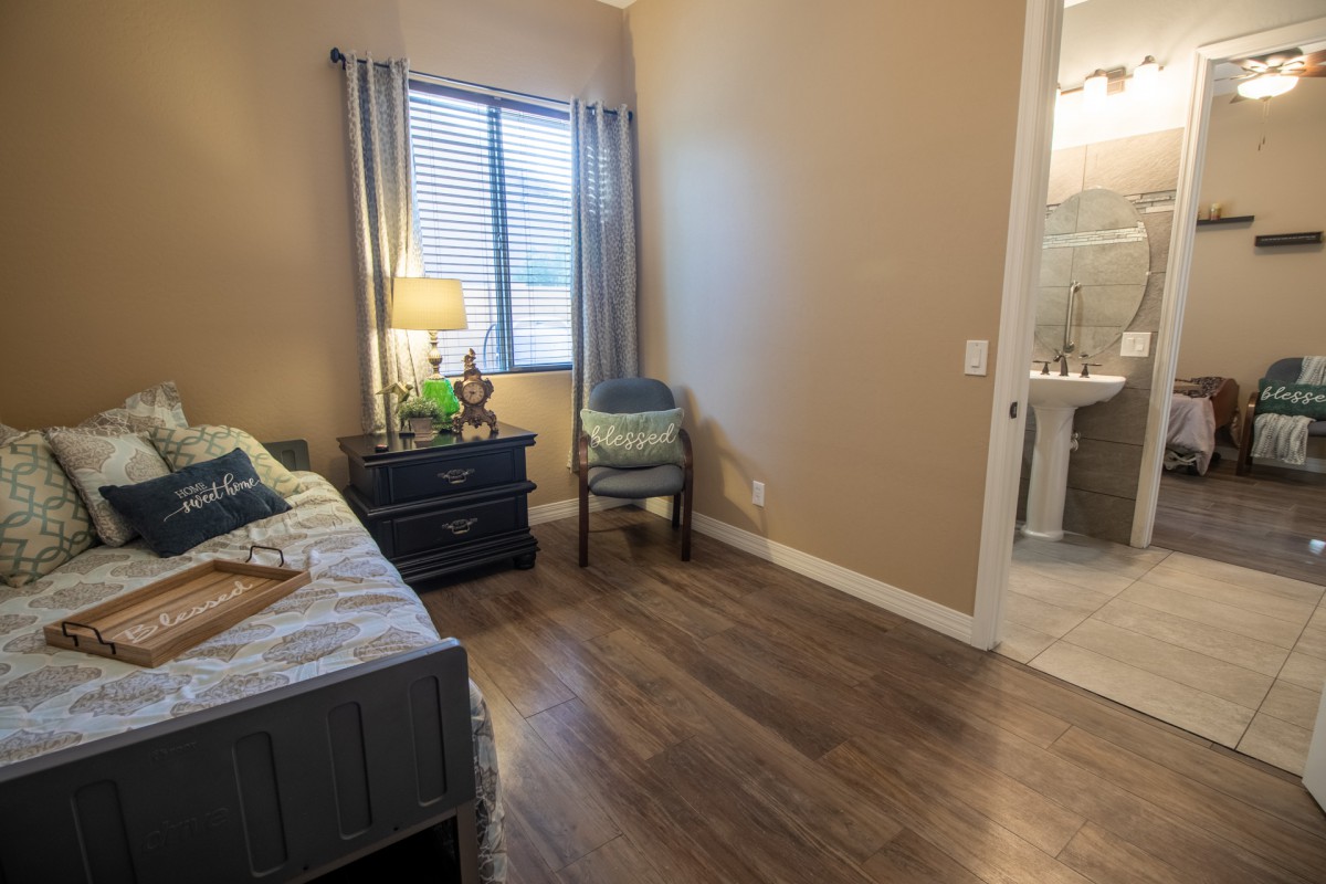 A cozy bedroom with wooden flooring, a comfortable bed, and a lamp by the window.