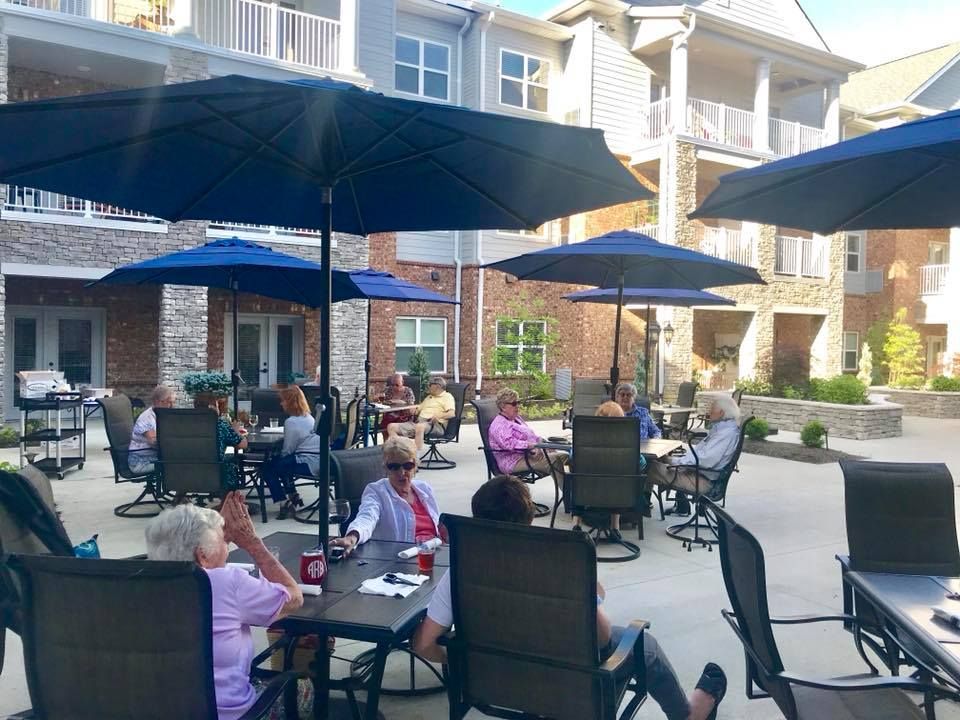 A group of people enjoying a social gathering on a sunny patio with umbrellas and seating.