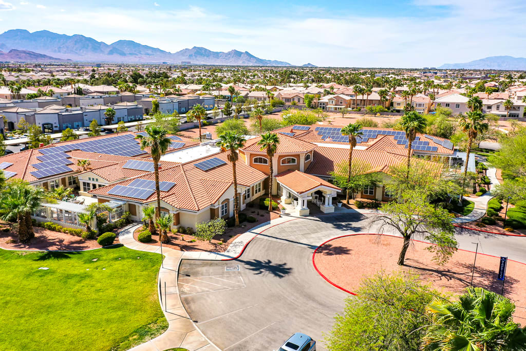 Aerial view of a suburban neighborhood featuring houses with solar panels, surrounded by palm trees and mountains under a clear sky.