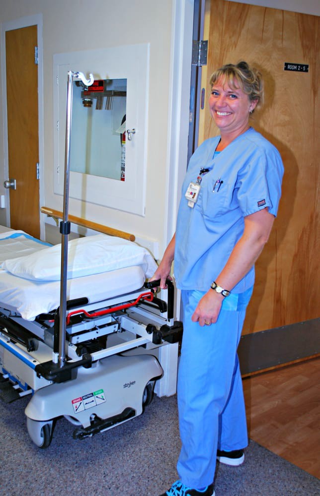 A nurse in blue scrubs standing next to a hospital gurney.
