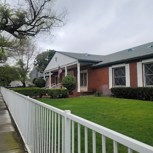 A charming brick house with a well-maintained lawn and white picket fence under a cloudy sky.