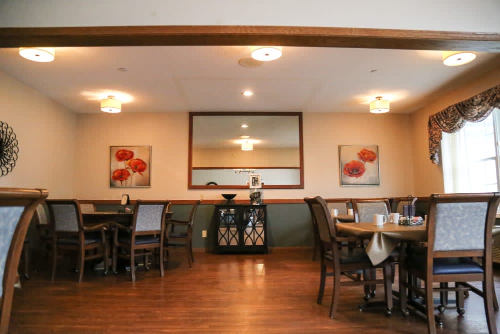 A cozy dining area with neatly arranged tables and chairs, complemented by decorative artwork and a large mirror on the wall.