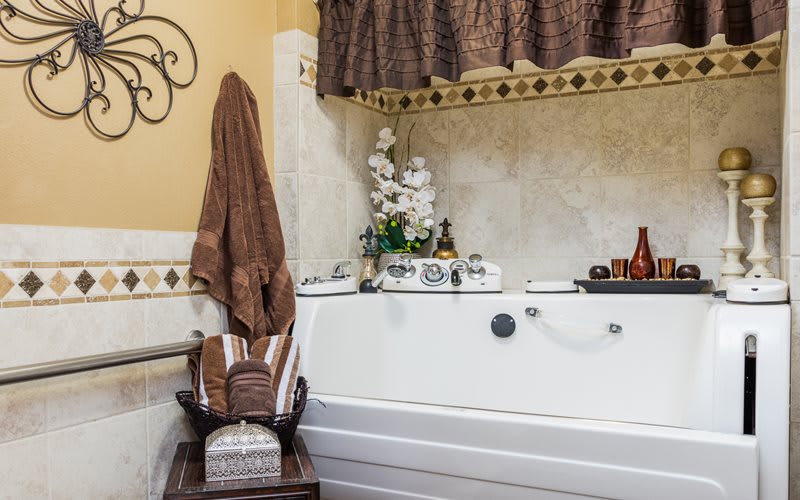 A cozy bathroom with a white tub, brown towels, decorative plants, and candles.
