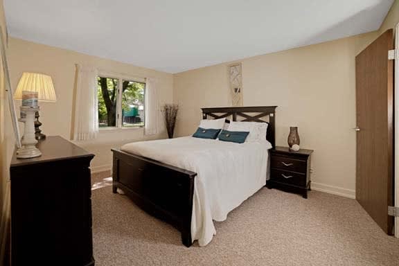 A cozy bedroom featuring a large bed with dark wooden frame, complemented by matching nightstands and a carpeted floor.