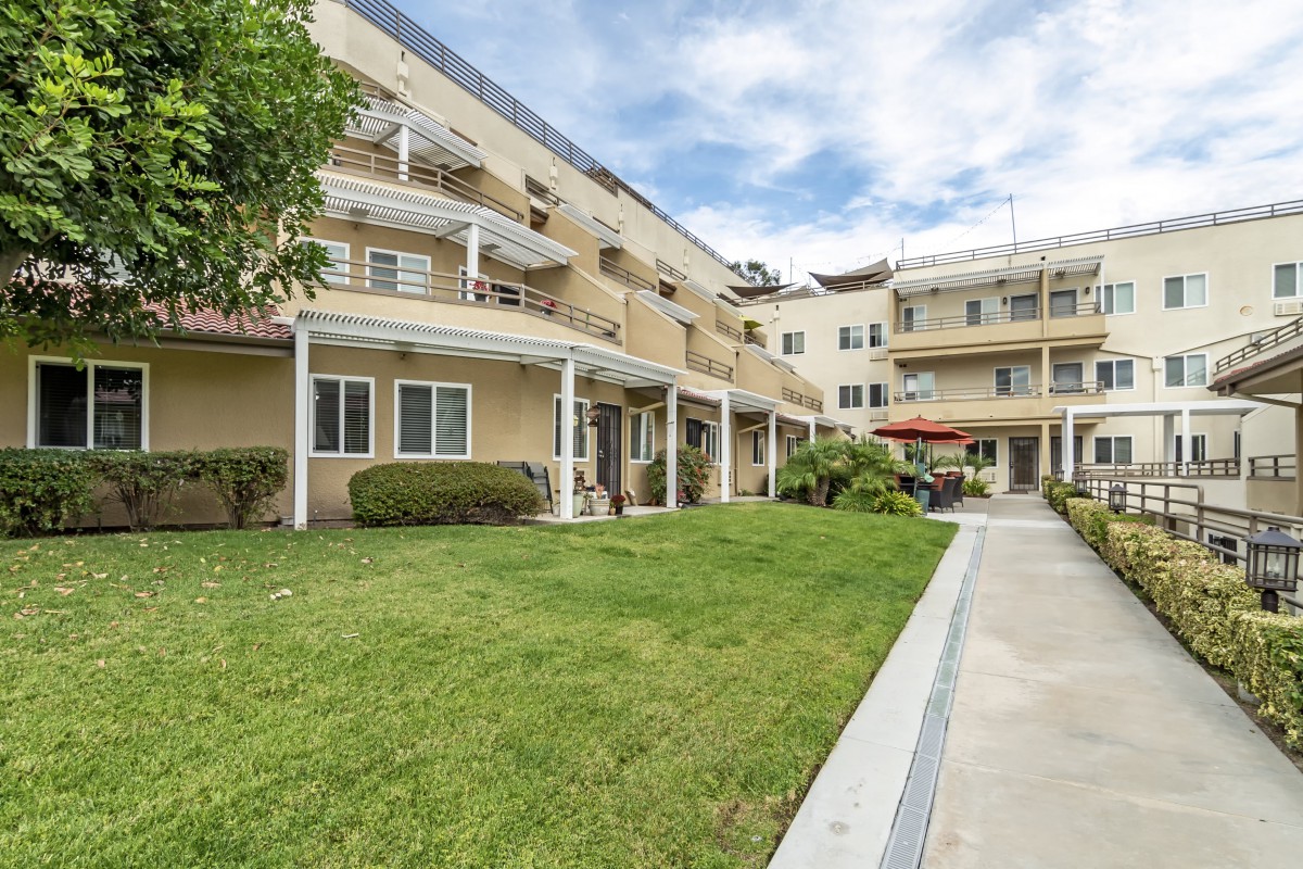 A residential apartment building with balconies overlooking a well-maintained lawn and garden path.
