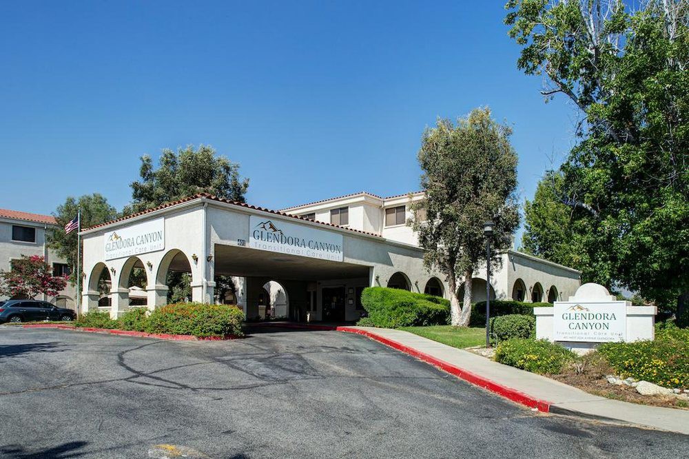 A hotel building with a driveway and arches surrounded by trees.