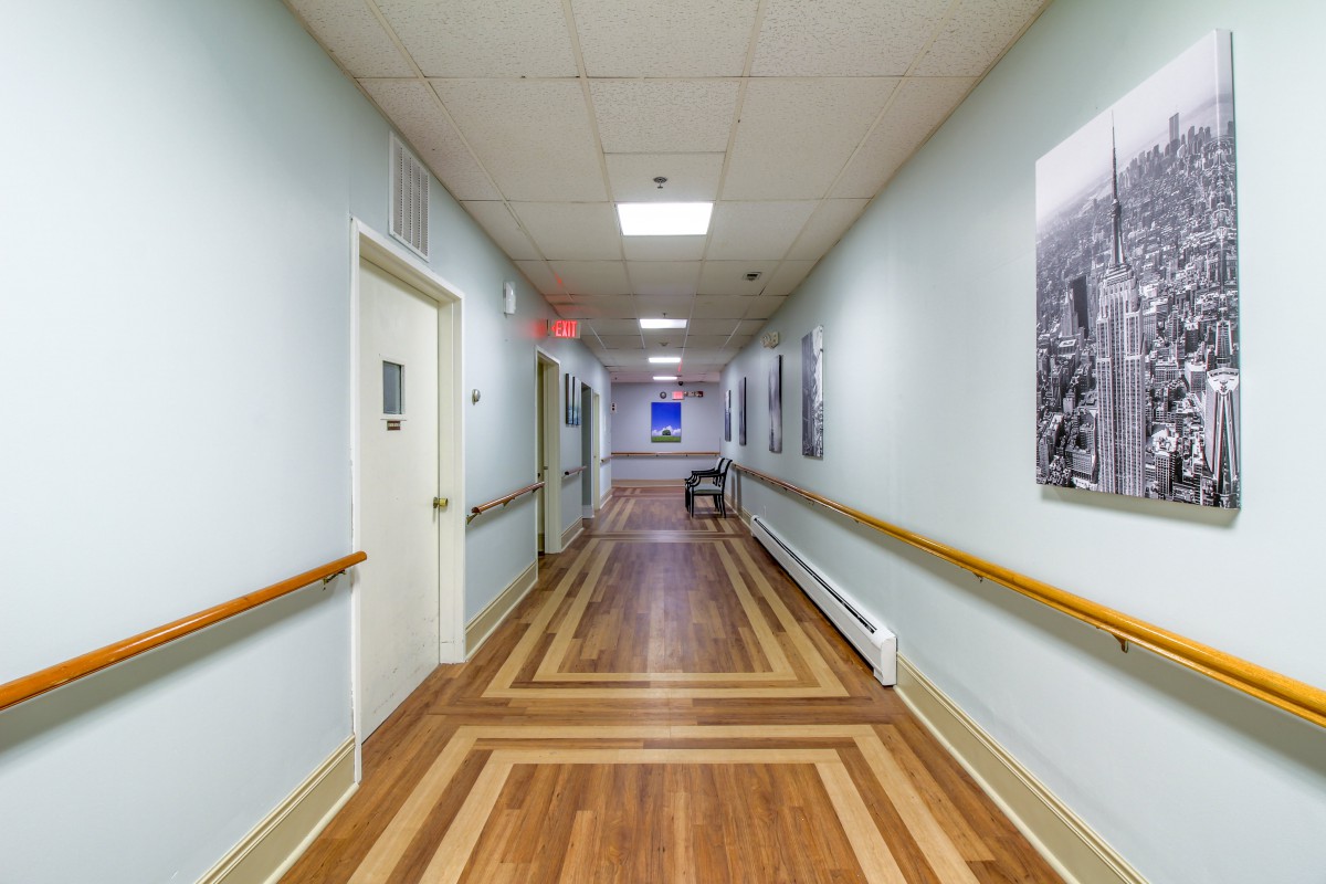 A long, empty hospital corridor with wooden flooring and bright lighting.