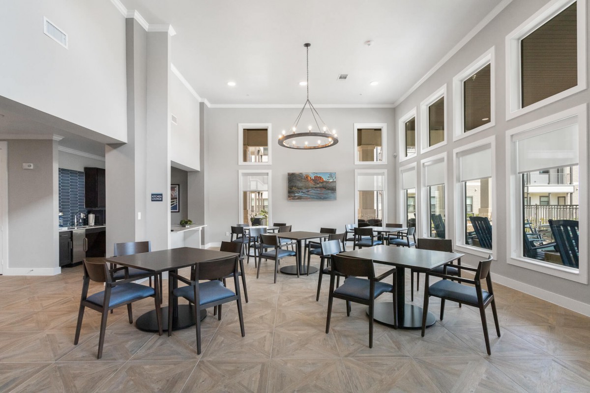 A modern dining area with tables and chairs, featuring large windows and a central lighting fixture.