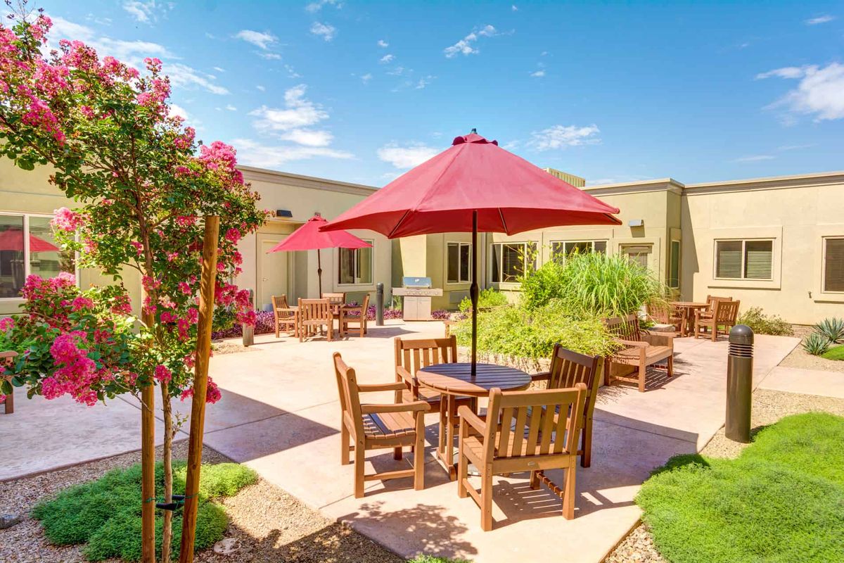 A sunny outdoor patio with wooden furniture and red umbrellas.
