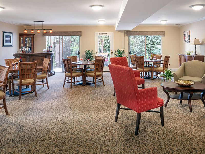A cozy dining area with tables and chairs, decorated with plants and large windows providing natural light.